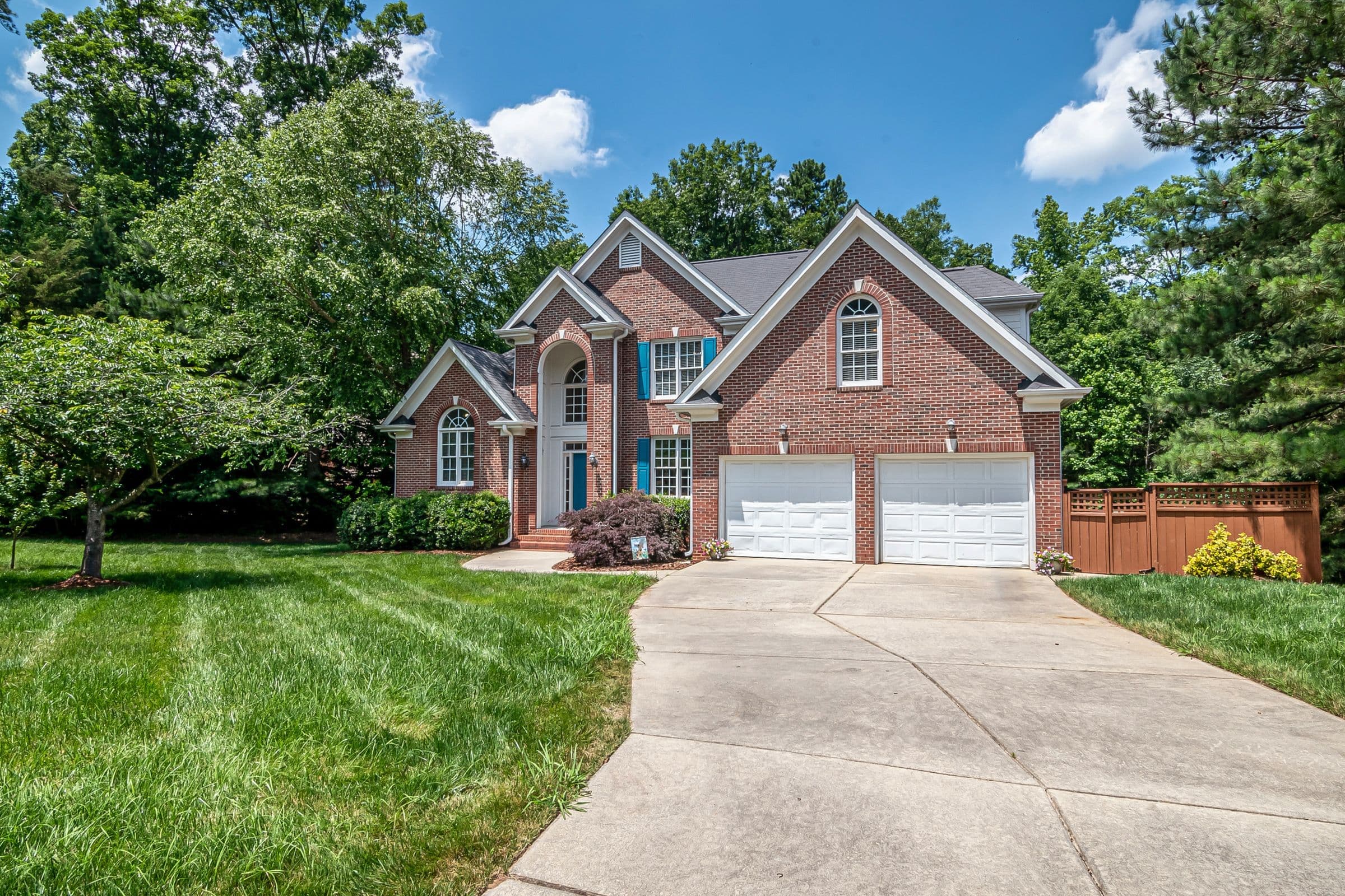 Junk removal in Farragut, TN: two-story brick house with a two-car garage, long driveway and mowed lawn in a wooded subdivision
