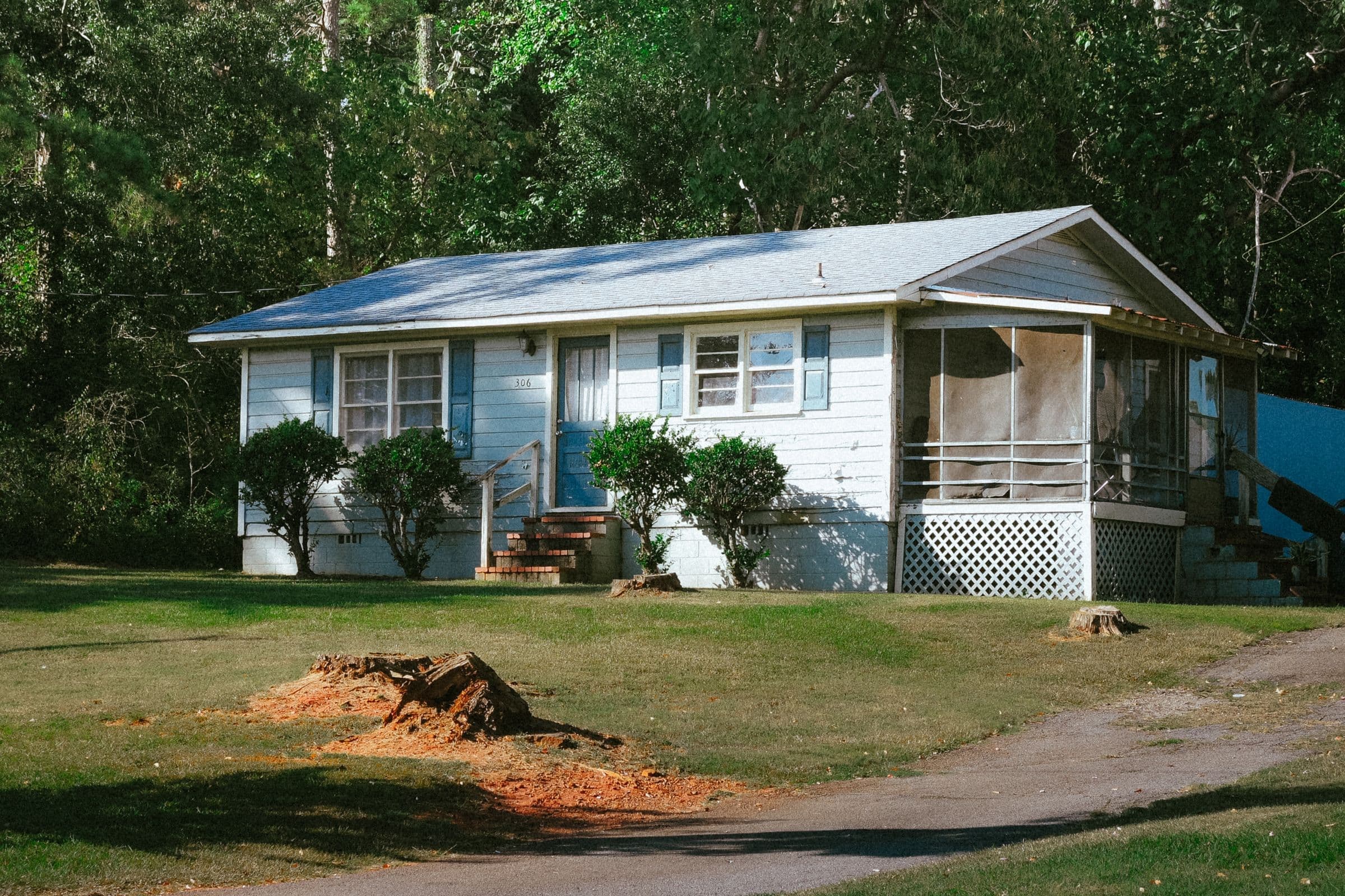 Junk removal in Powell, TN: small one-story ranch house with blue shutters and a screened porch in front of thick woods